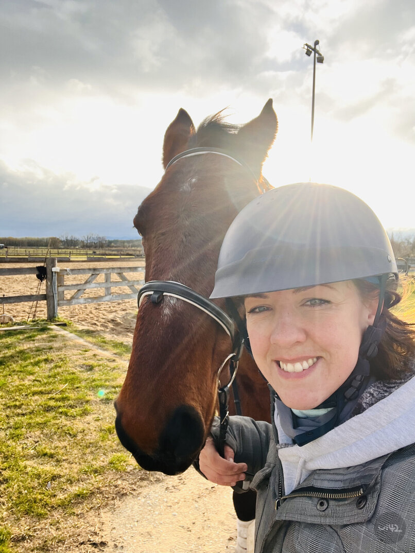 The woman in a riding helmet poses with a horse on a sunny day at the farm.